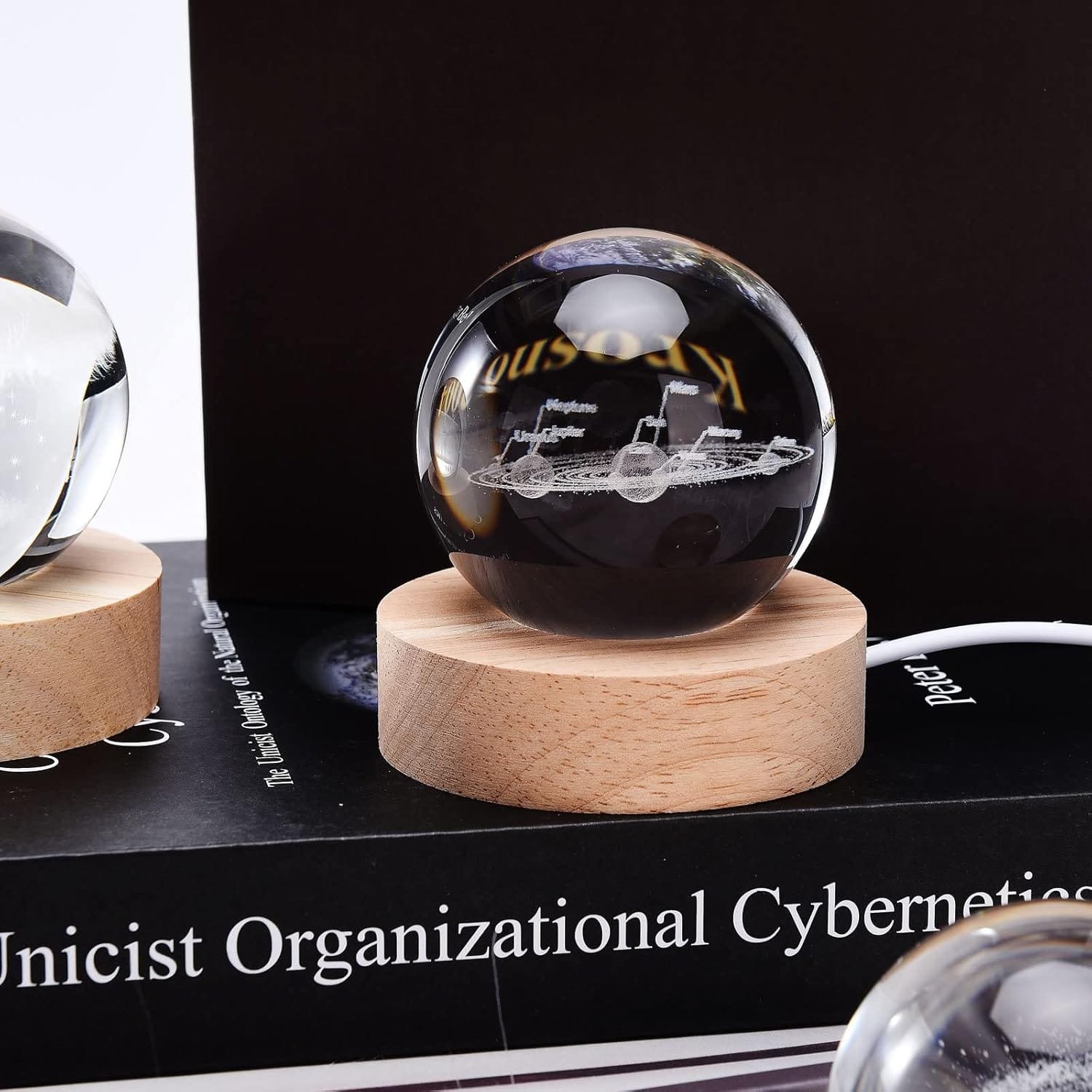 A crystal sphere with an engraved ship sits on a wooden base, placed on a book titled "Unicist Organizational Cybernetics.