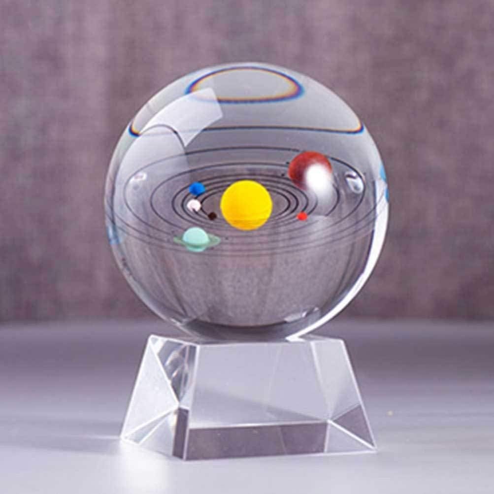 A glass sphere displaying a miniature solar system model on a clear, faceted stand against a blurred background.