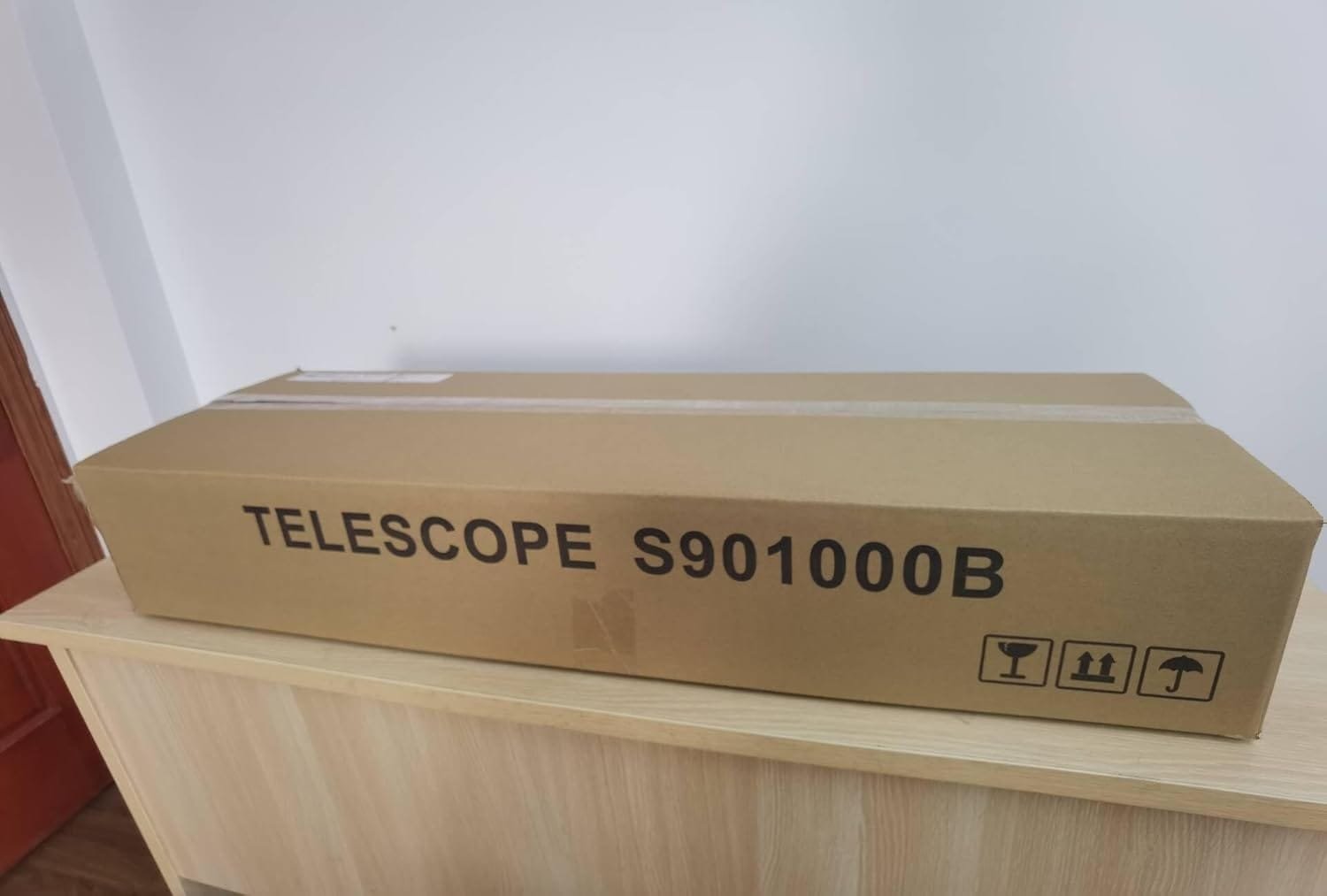 Cardboard box labeled "TELESCOPE S901000B" on a wooden surface.
