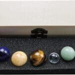 A set of nine polished gemstone spheres arranged in a black foam tray inside an open wooden box.