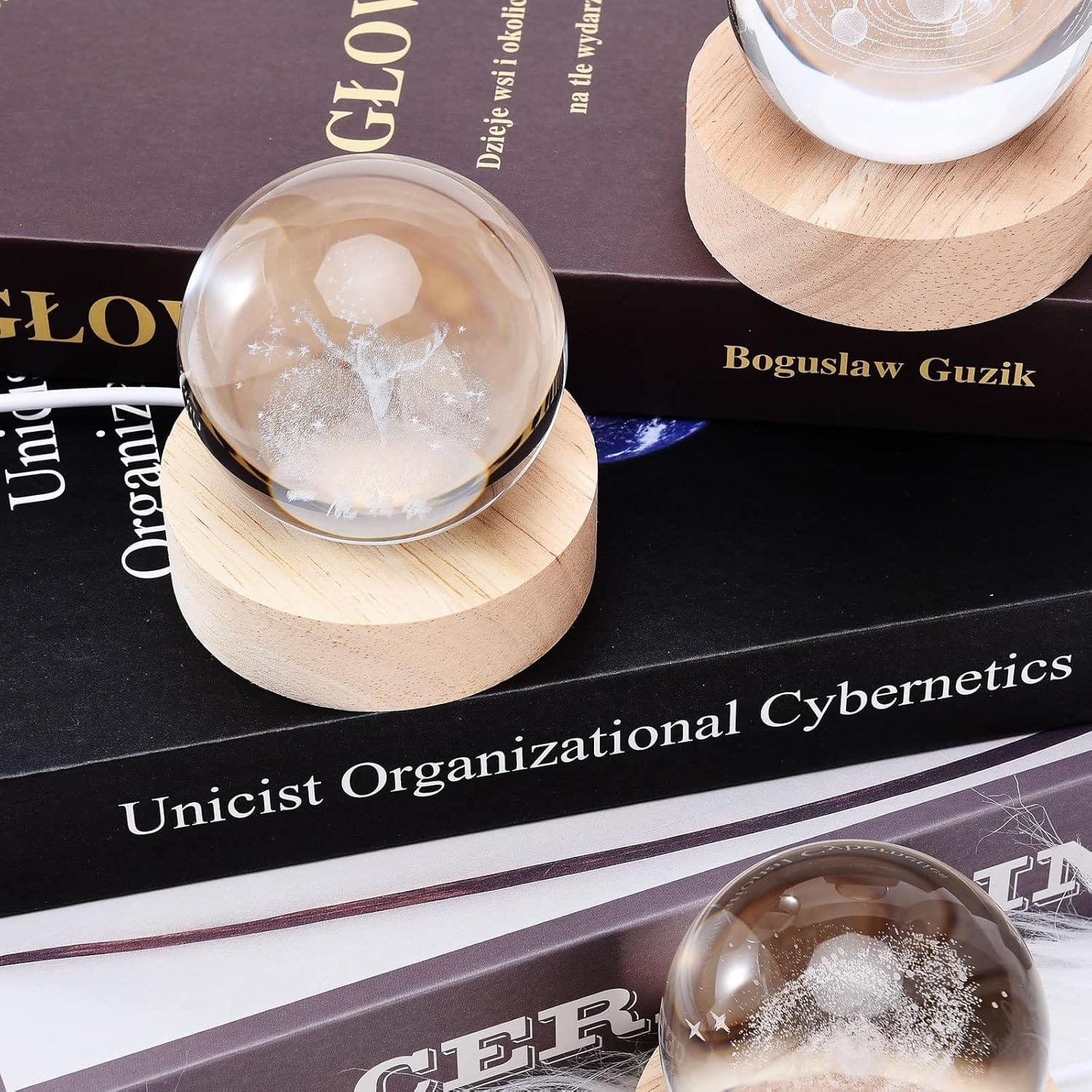 Crystal spheres on wooden stands placed on stacked books. Titles include "Unicist Organizational Cybernetics" and "Bogusław Guzik.