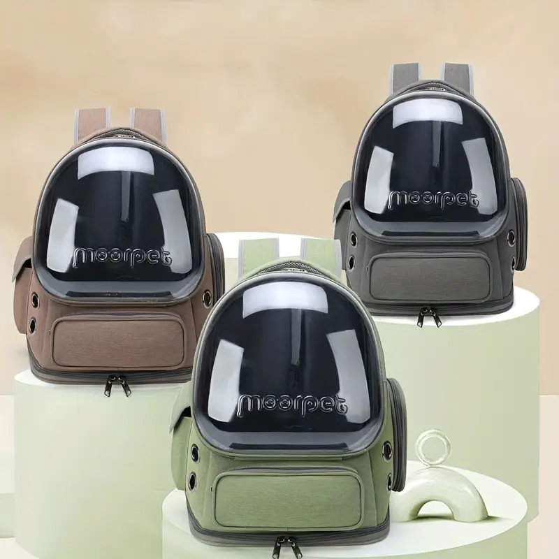 Three pet carrier backpacks in brown, gray, and green with transparent domes are displayed on rounded platforms against a beige background.