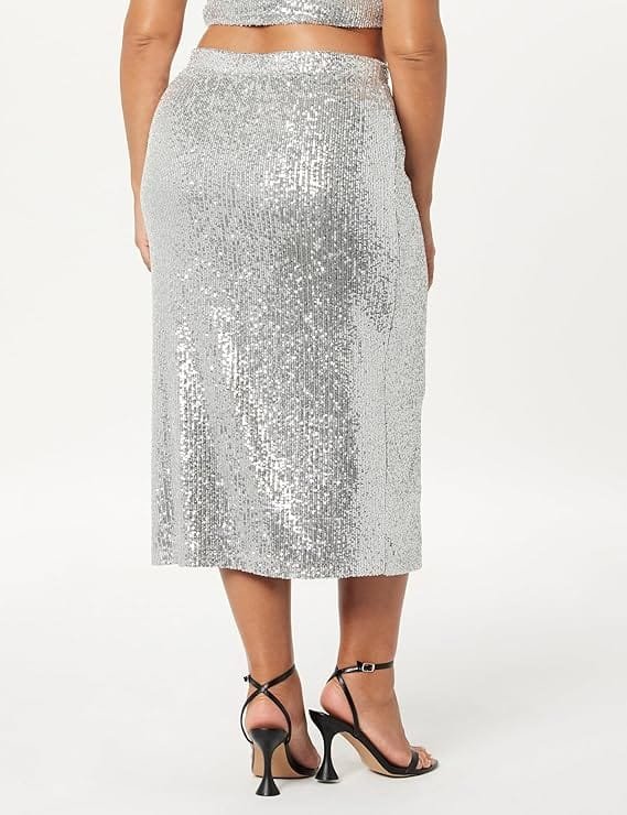 A person wearing a silver sequined skirt and black strappy heels is standing with their back facing the camera.