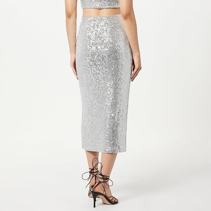 A woman standing with her back to the camera, wearing a silver sequin skirt and strappy black high-heeled sandals.