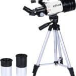 A white and black telescope mounted on a silver tripod stands next to two interchangeable eyepieces on a white background.