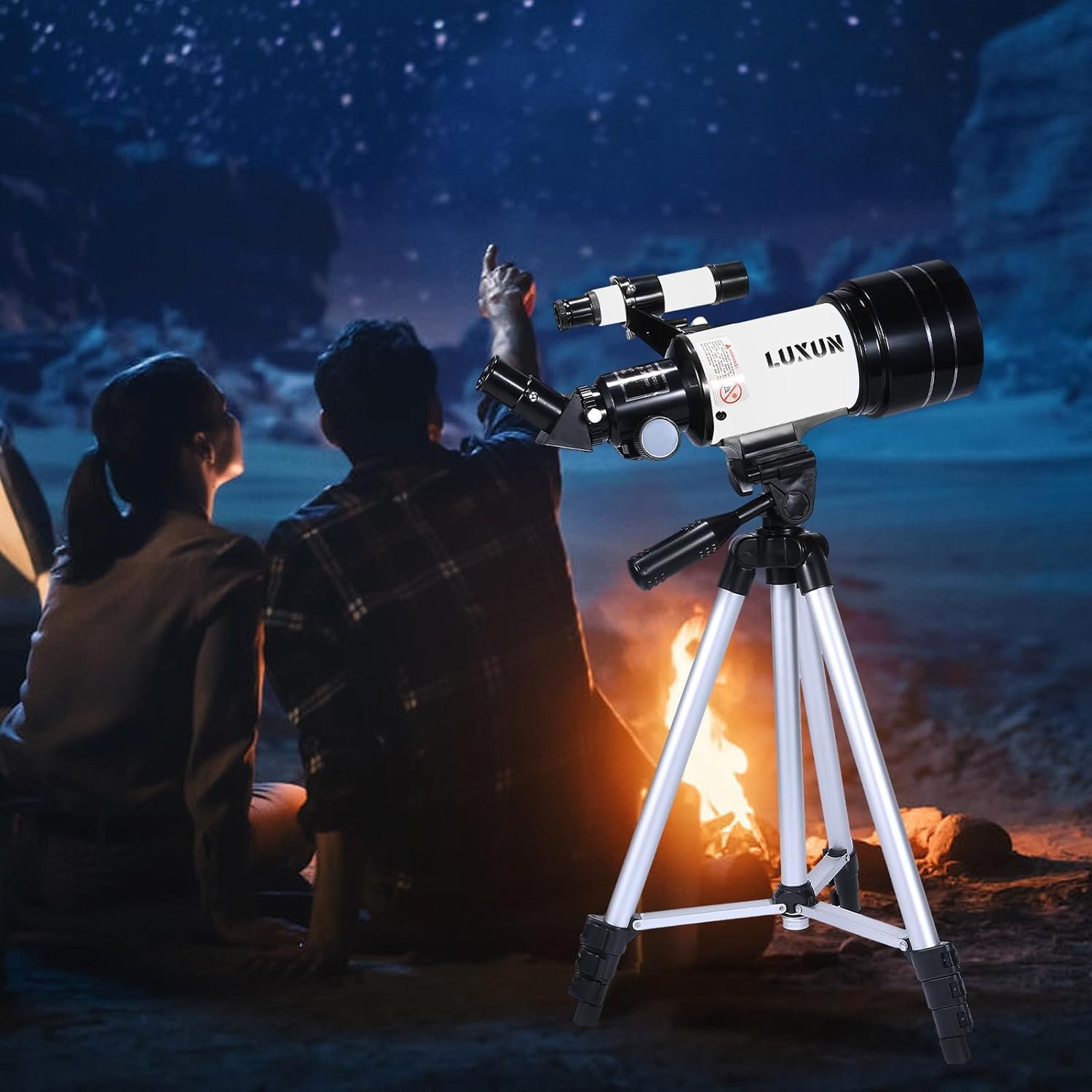 A telescope on a tripod stands in the foreground while two people sit by a campfire under a starry night sky, one pointing upward.