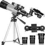 A black and gray telescope mounted on a tripod, with a smartphone adapter attached, and three additional eyepieces displayed nearby.