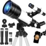 A black and white telescope on a tripod with eyepieces, a finder scope, phone adapter, and a smartphone displaying an image of Jupiter.