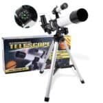 A white astronomical telescope with black accents is mounted on a silver tripod next to its packaging box, which shows an image of the telescope and space-themed graphics.