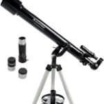 A black Celestron refractor telescope on a white tripod, with three interchangeable eyepieces placed nearby.