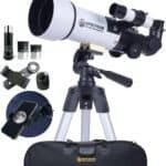 A white and black telescope on a tripod with accessories including eyepieces, a phone mount, a bag, and a close-up image of the moon on a smartphone screen.
