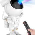 A hand holds a remote control pointed at a small astronaut figurine, which is projecting colorful lights from its helmet.