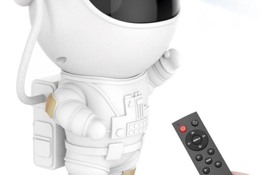 A hand holds a remote control pointed at a small astronaut figurine, which is projecting colorful lights from its helmet.