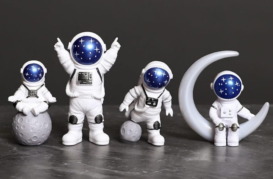 Four astronaut figurines with blue, starry helmets are posed on and around gray moon props against a dark background.