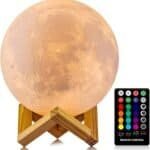 A moon-shaped lamp on a wooden stand is shown next to a remote control with various color and brightness options.