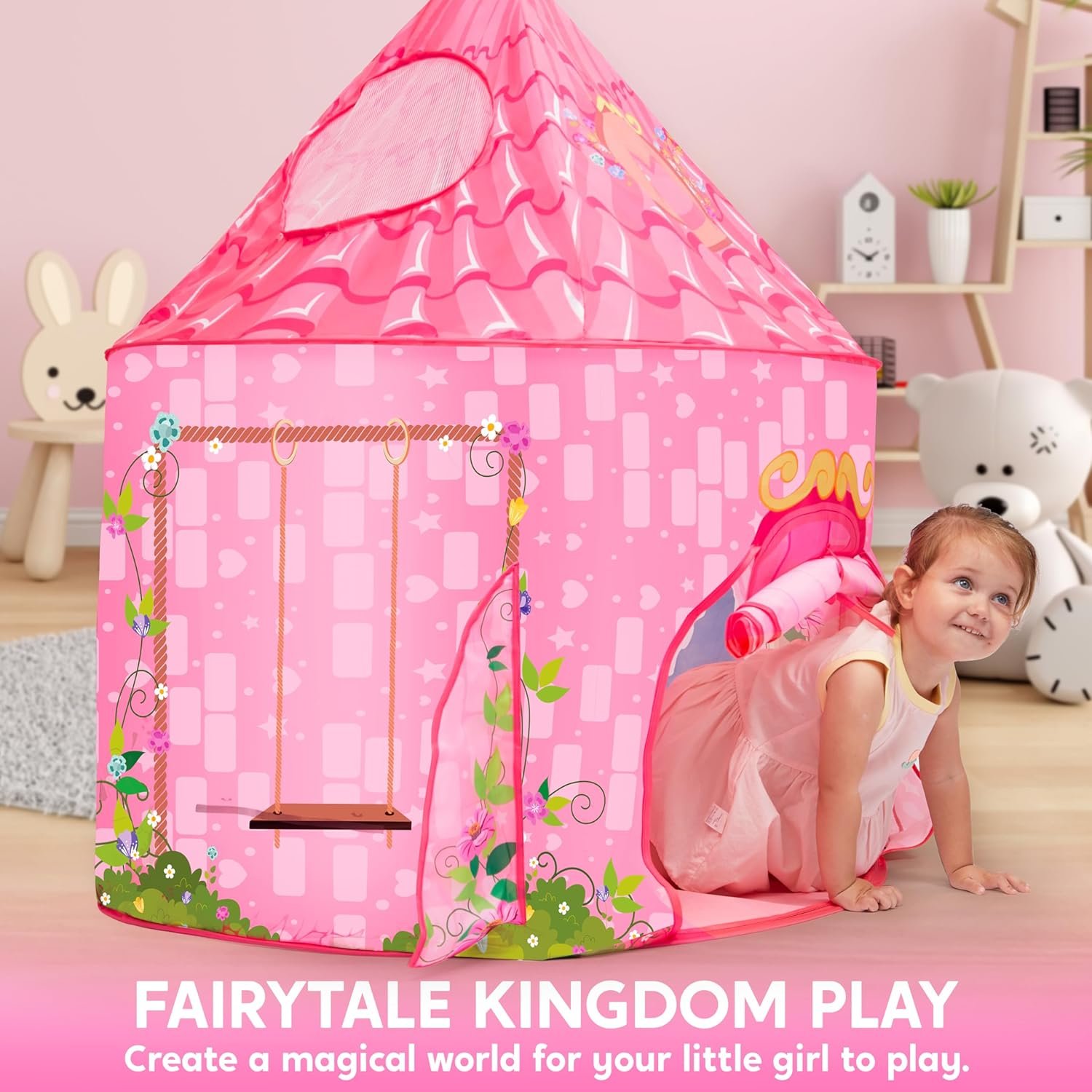 A young girl in a pink dress crawls out of a pink fairytale-themed play tent inside a child's room, with stuffed animals and toys in the background.