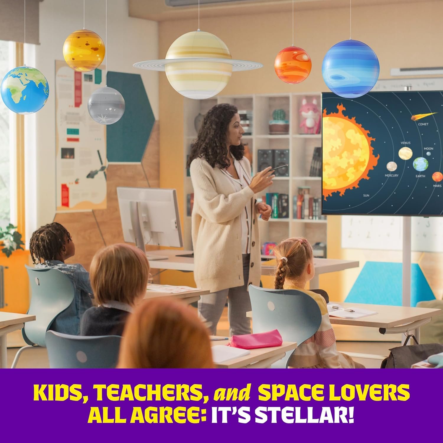 A teacher presents a solar system diagram to students in a classroom decorated with hanging planet models and a yellow banner with STEM-themed text.