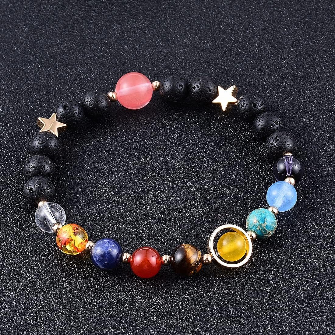 A beaded bracelet with multicolored round stones, black beads, two gold star charms, and a circular gold accent, displayed on a black textured surface.
