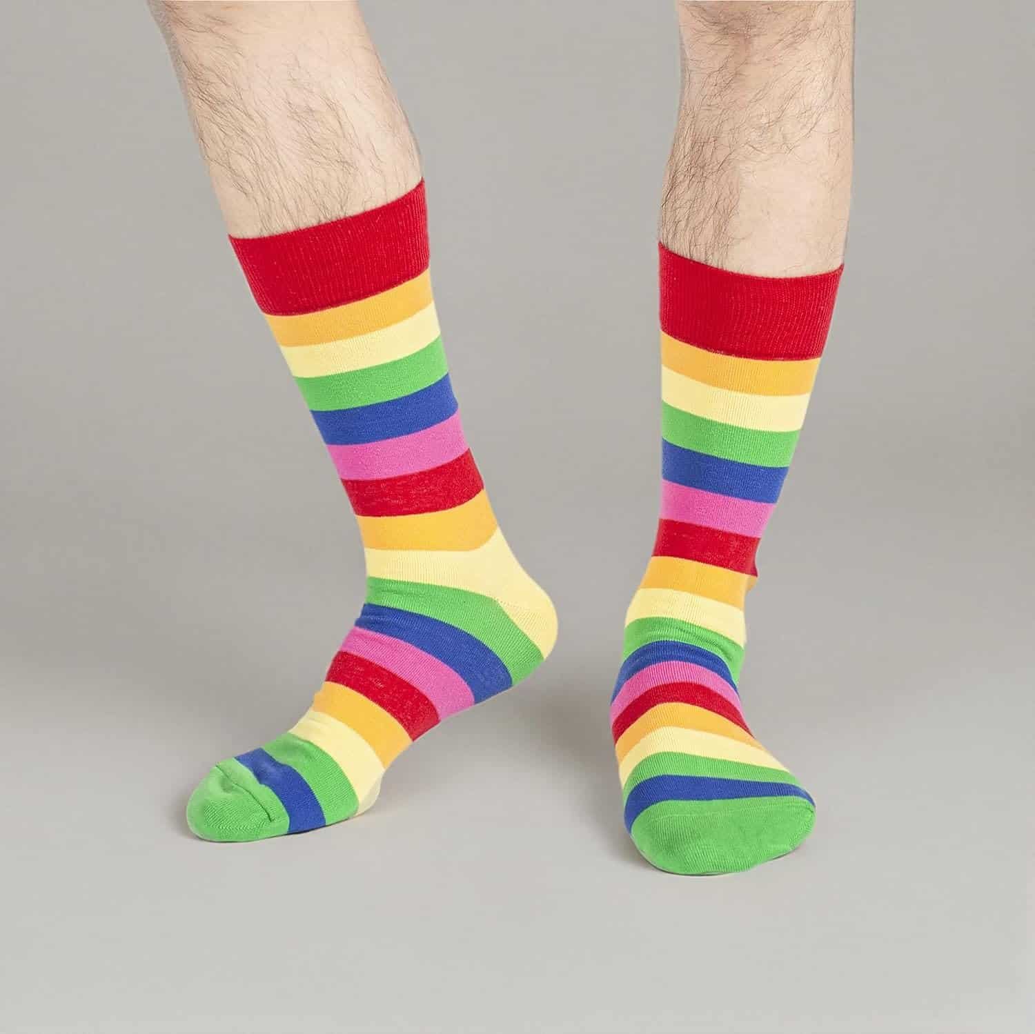 Person wearing knee-length socks with horizontal rainbow stripes, standing on a plain grey background.