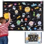A young child interacts with a colorful felt board displaying cartoon representations of the solar system and planets, with an educational kit shown in the corner.