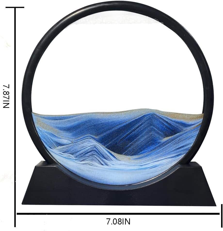 A round sand art sculpture with blue and white layers creating wave patterns, set on a black base. Dimensions are 7.87 inches tall and 7.08 inches wide.