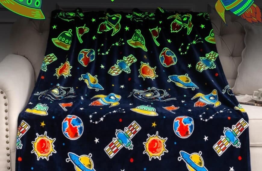 A dark-colored blanket with colorful space-themed designs, including planets, rockets, UFOs, suns, satellites, and stars, draped over a light-colored sofa.