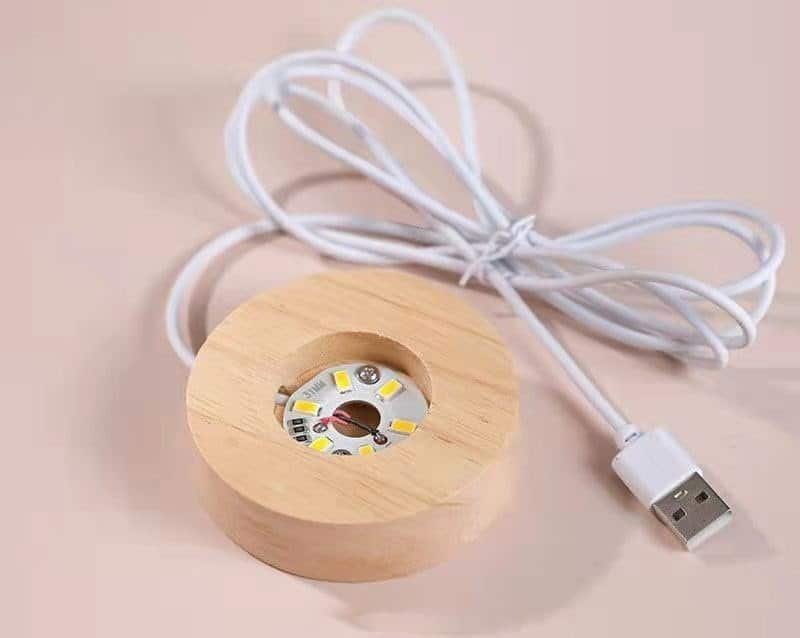A round wooden LED light with a white USB cable attached, lying on a light surface.