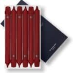 Six red double-ended markers are arranged in a white box, placed on top of a dark blue rectangular item with text partially visible in the corner.