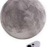 A grey, textured, spherical object resembling the moon is shown next to a small white remote control with two buttons.