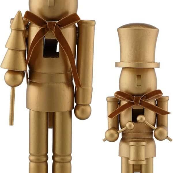 Two gold-painted wooden nutcracker figures, one taller with a crown and a tree, the other shorter with a top hat, both standing on rectangular bases and wearing brown ribbon bows.