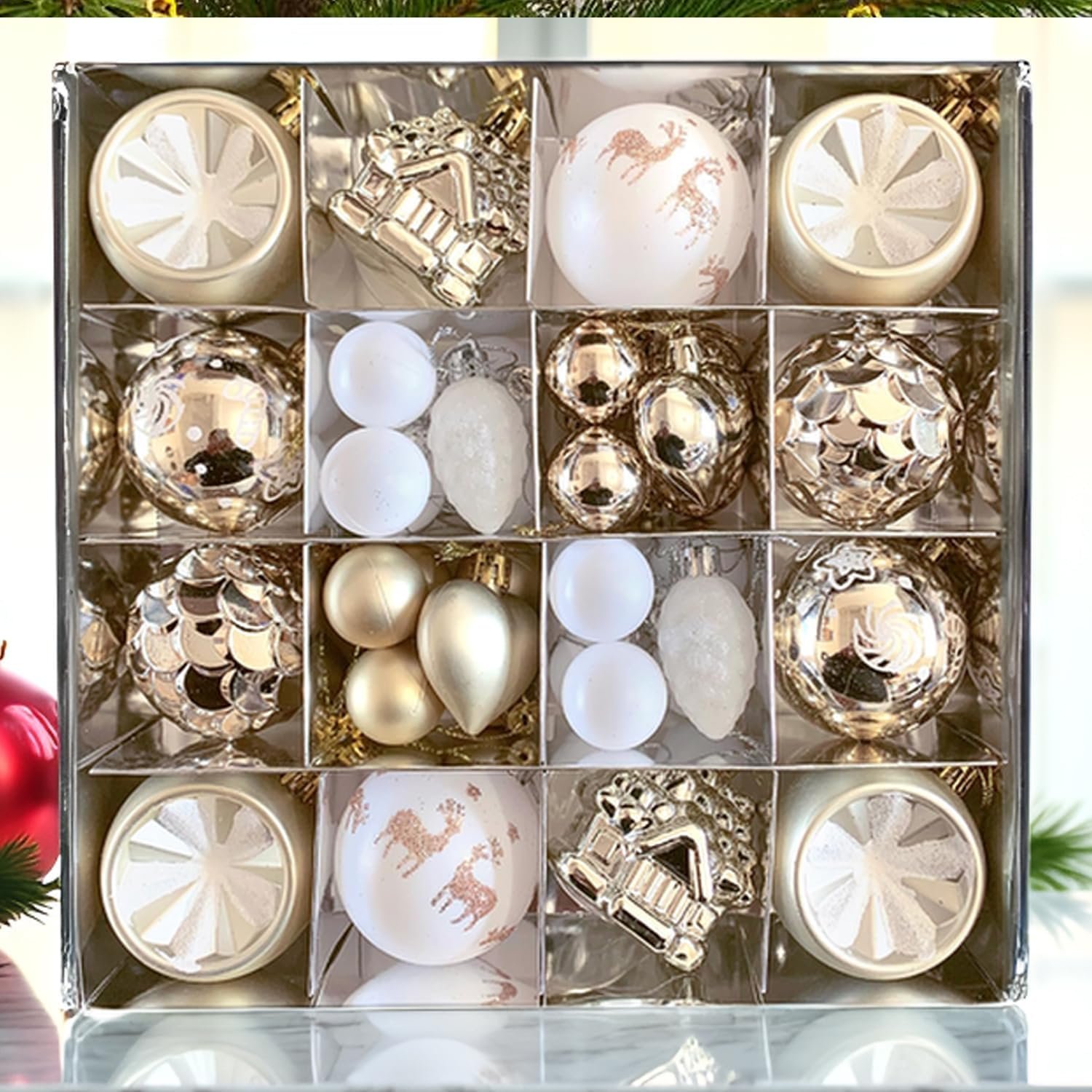 A box with sixteen compartments containing assorted gold and white Christmas tree ornaments in various shapes and designs.