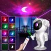 A person uses a remote to control an astronaut-shaped projector that casts colorful galaxy and moon patterns on a living room ceiling.