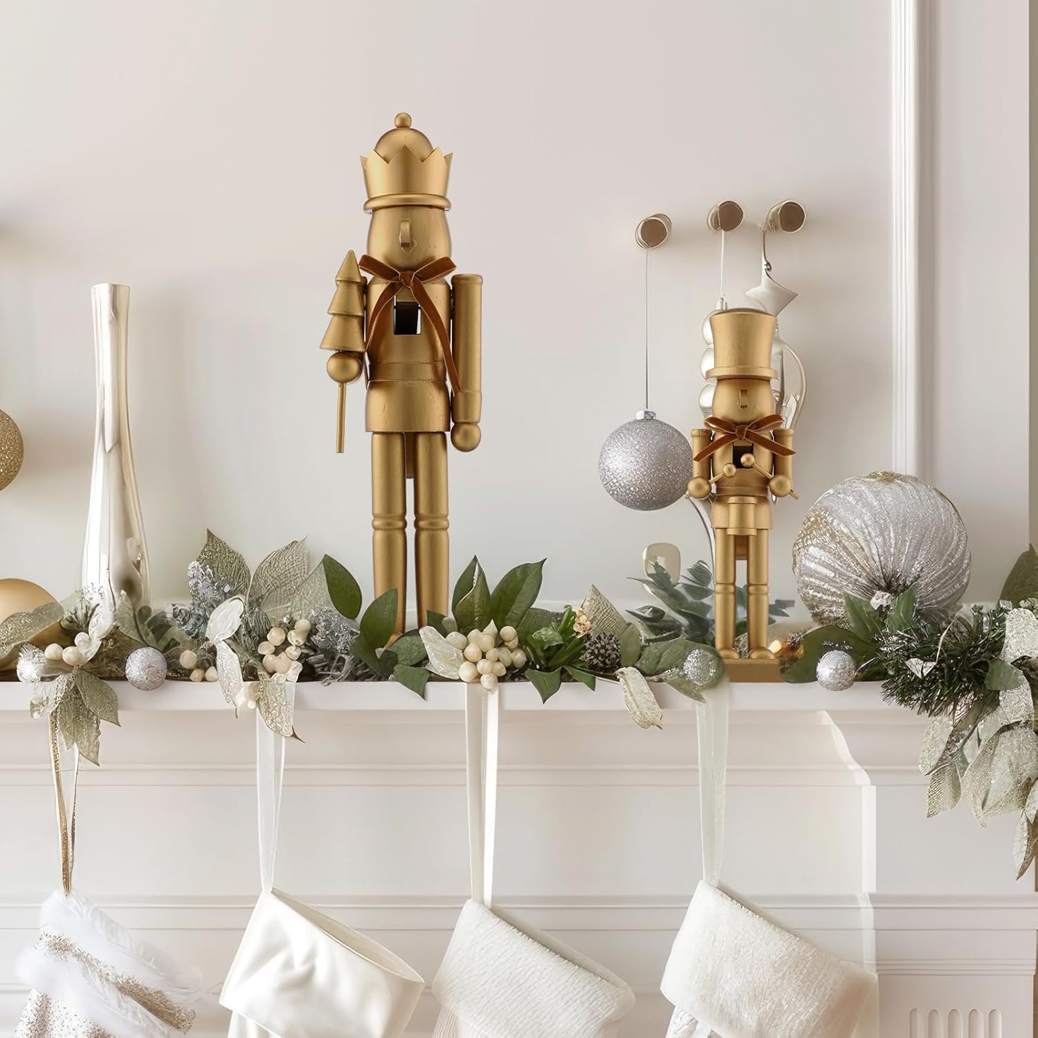 Two gold nutcracker figures and silver ornaments are displayed on a decorated mantel with greenery and white stockings hanging below.