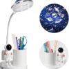 A white desk lamp with a flexible neck projects a starry sky pattern, featuring a built-in pen holder and a small astronaut figure attached to the base.