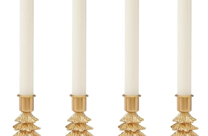 Four white taper candles lit and placed in gold holders shaped like Christmas trees, aligned in a row against a white background.