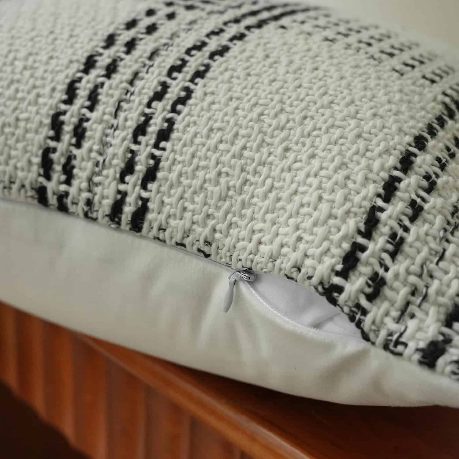 Close-up of a textured cream and black striped pillow with a visible zippered opening on one side, resting on a wooden surface.