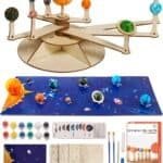 A DIY solar system model kit with painted and unpainted planet spheres, brushes, paint pots, wooden assembly pieces, instruction cards, and a colorful planet mat displayed.