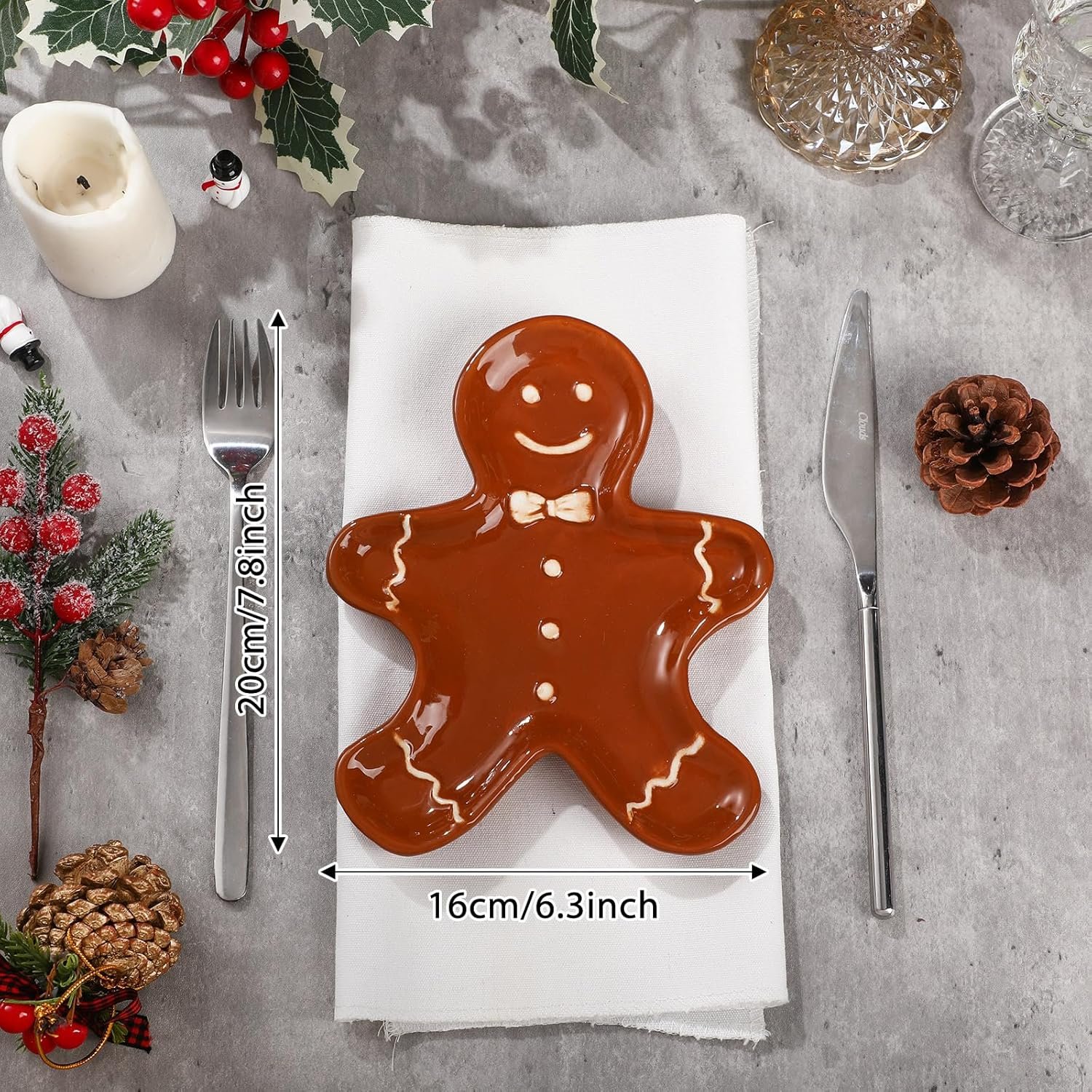 A gingerbread man-shaped plate on a white napkin is set between a knife and fork, with size dimensions shown; holiday decorations surround the arrangement.