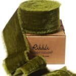 A roll of olive green velvet ribbon is partially unspooled and displayed on a brown cardboard box labeled “Ribbli.”.