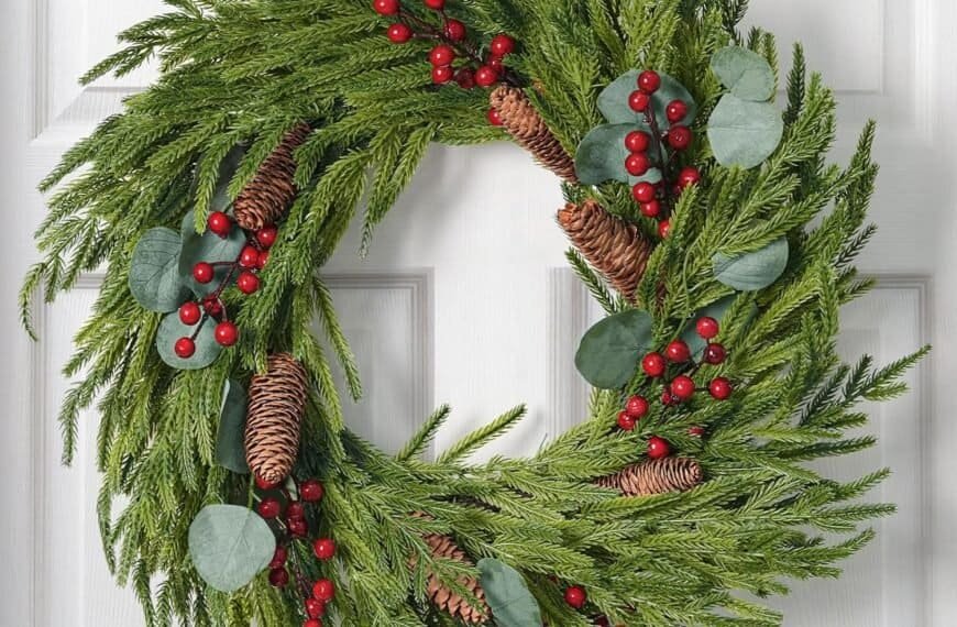 A green holiday wreath with pinecones, red berries, and eucalyptus leaves hangs on a white door.