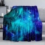A blue and purple galaxy-patterned blanket is draped over a gray sofa in a modern living room.