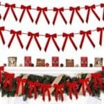 Red bows hanging on two strings, with additional red bows decorating a fireplace mantel adorned with greenery, red candles, wrapped logs, pinecones, and other festive ornaments.