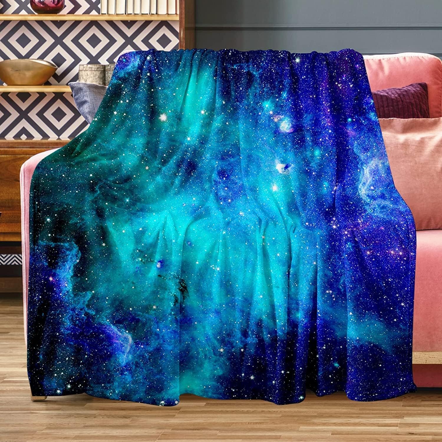 A blue and green galaxy-themed blanket with star patterns draped over a pink sofa in a living room setting.