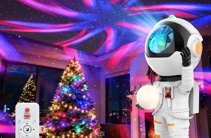 A Christmas tree with presents sits beside a Rossetta Astronaut Galaxy Projector, casting colorful lights on the ceiling, while its remote rests in the foreground, creating playful room decor perfect for Christmas or birthday gifts.