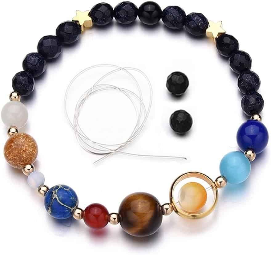 A beaded bracelet with colorful planet-like beads, gold accents, star-shaped beads, a spare wire, and two extra black beads displayed on a white background.