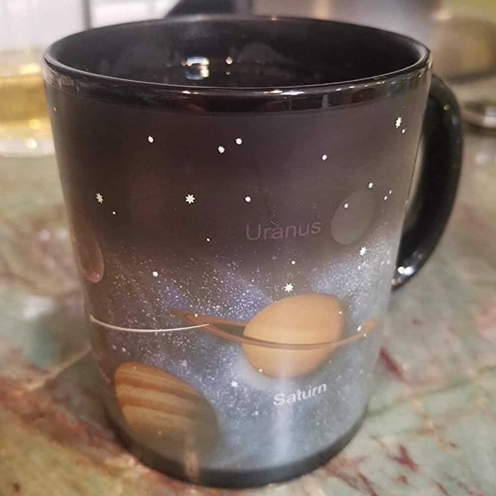 A black mug featuring an illustration of planets, labeled "Uranus" and "Saturn," with stars and a galaxy in the background.