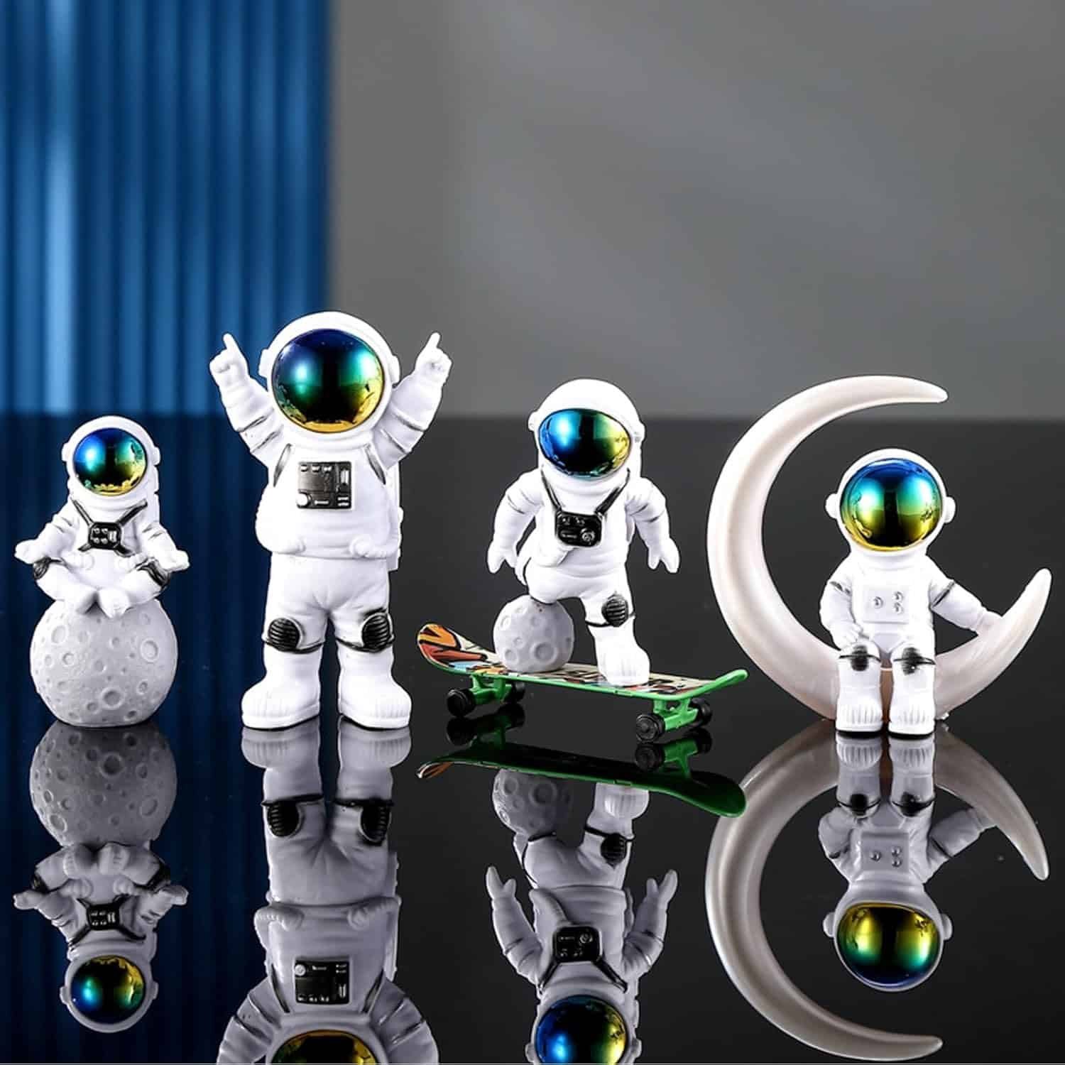 Four astronaut figurines are posed on a reflective surface, with two sitting on moons, one on a crescent moon, and one standing beside a skateboard. A blue background is partially visible.