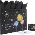 A black gift bag with a space-themed design and "Happy birthday to you" text, black tissue paper, and a matching birthday card with envelope.