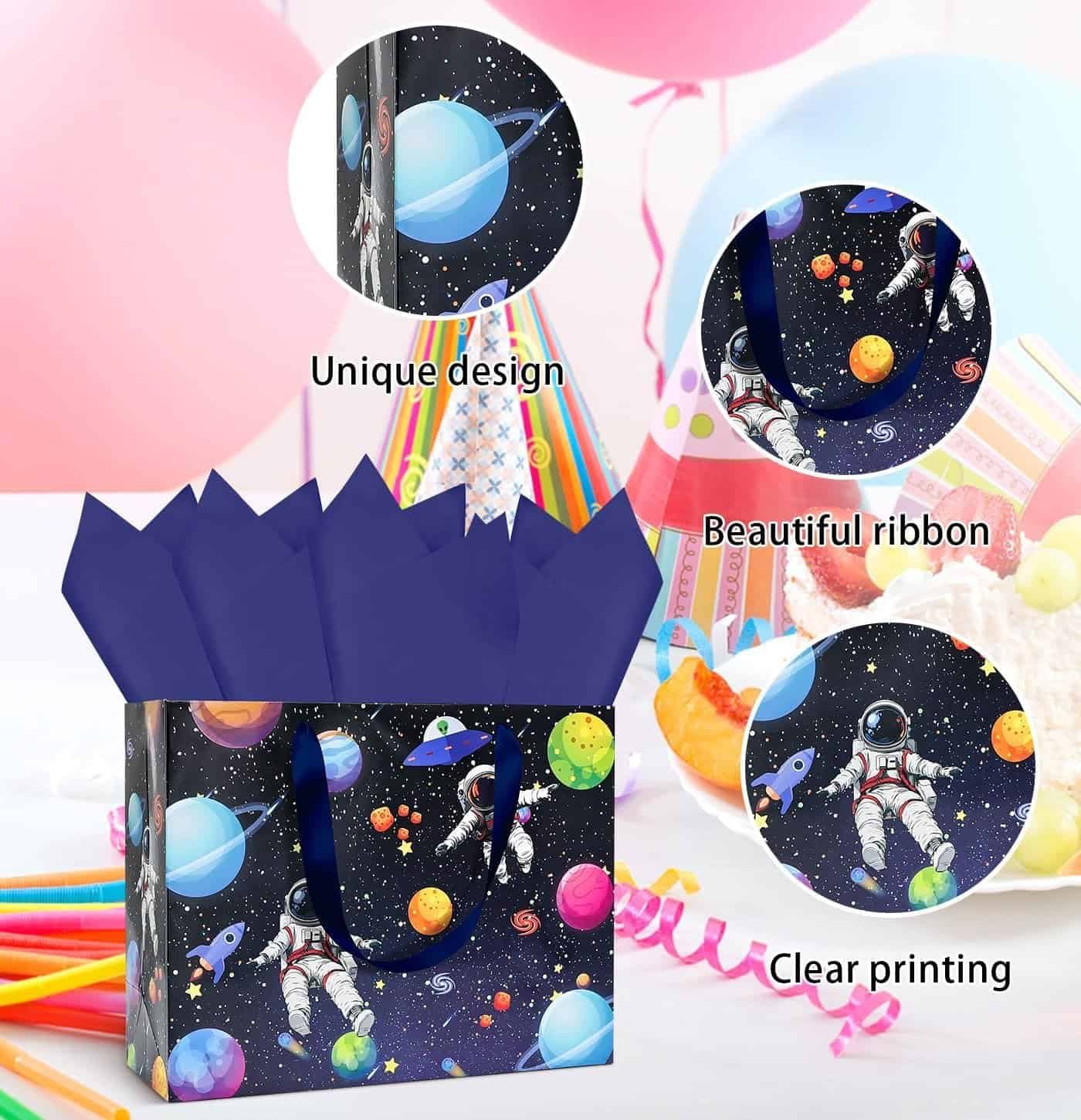 Gift bag with an outer space and astronaut design, blue ribbon handles, and dark blue tissue paper, surrounded by balloons, party hats, and desserts.