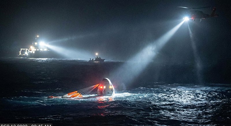 At night, a rescue helicopter shines a spotlight on a partially sunken vessel in rough seas, with rescue boats and a ship nearby providing assistance—an operation reminiscent of NASA’s precise coordination during critical missions.